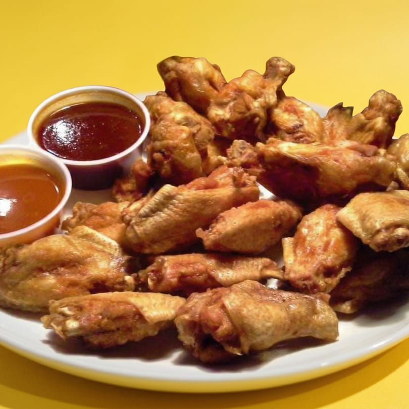 A white plate piled high with crispy chicken wings and two small cups of dipping sauces.
